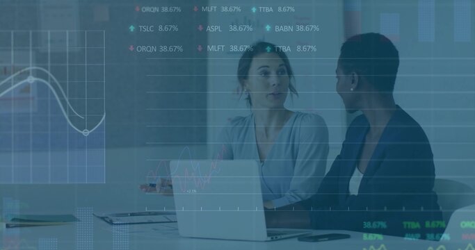 Talking two women in business clothes reviewing data charts at meeting table, with laptop - Powered by Adobe