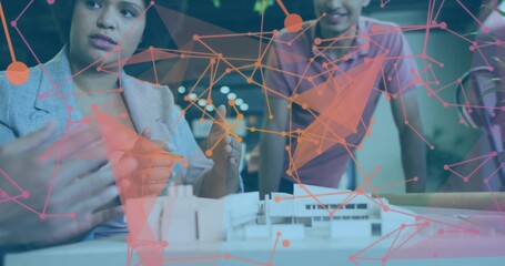 Examining blazer-clad woman and collared man leaning over scale model in studio with pink-orange AR