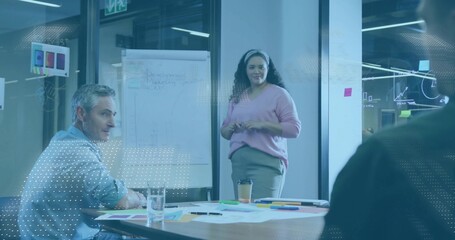 Presenting female speaking and gesturing toward flip chart in conference room, pink sweater, papers
