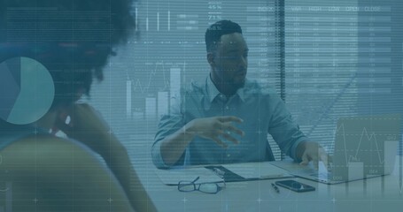 Gesturing man in light shirt presenting chart overlays at meeting table, referencing laptop