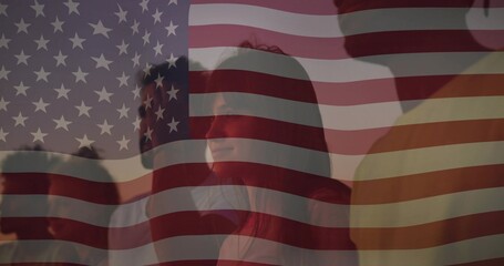 Watching group of adults standing behind sheer American flag at sunset, wearing casual clothes