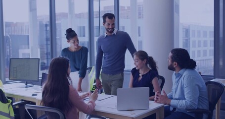 Reviewing plans, team wearing business-casual leaning over meeting table, laptop and safety vests