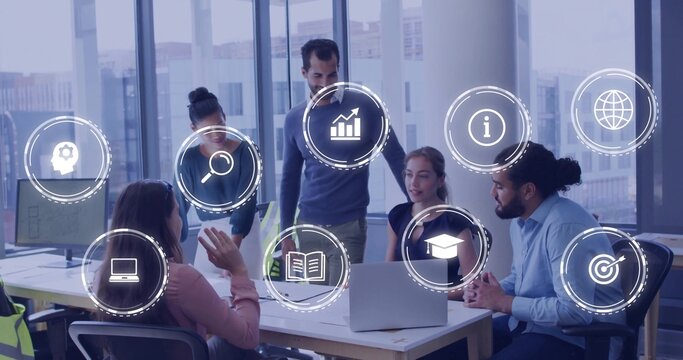 Discussing five staff wearing business-casual leaning around office table with laptop, papers