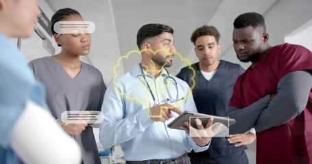 Pointing doctor showing tablet in hospital corridor with stethoscope, team in scrubs viewing UI