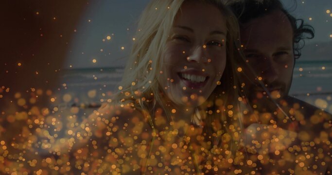 Smiling mid adult woman and younger man posing on sandy shore, wearing beachwear, golden bokeh - Powered by Adobe