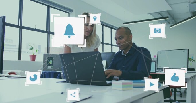 Collaborating coworkers in business attire leaning over laptop at office with digital icons