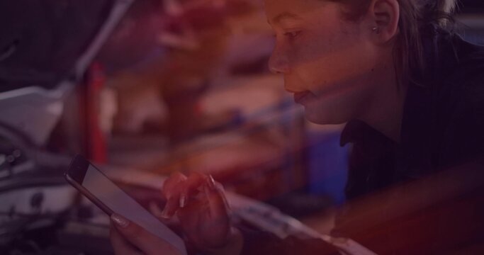Leaning woman tech examining engine with open hood while tapping tablet at garage, in dark jacket
