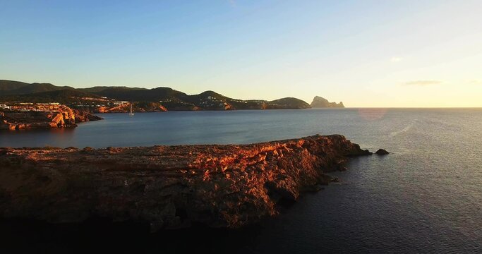 Framing rocky promontory stretching into calm sea from aerial viewpoint, distant headlands glinting