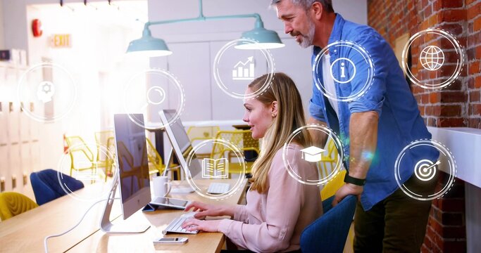 Typing woman in light pink blouse using desktop in open-plan office, man in blue shirt guiding - Powered by Adobe