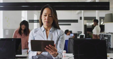 Reading woman holding tablet and reading screen in office, wearing light blue shirt