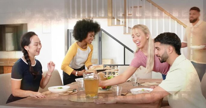Friends gathering around wooden table preparing food as woman entering carrying salad and bread