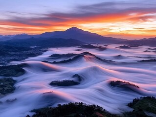 A breathtaking aerial view of rolling mountains shrouded in a thick sea of clouds during a vibrant sunrise, with a distant town visible.