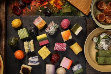 Traditional Malaysian desert Nonyah Kuih making preparing ingredients panadn leaf shredded coconut gula melaka  agar agar sagu spread over black slate messy rustic wood