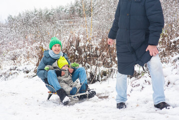 A happy teenage boy sits with his baby brother on a sled. Dad takes the children sledding in a snowy park.