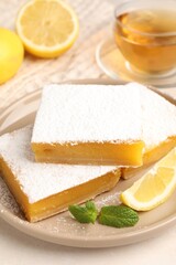 Tasty lemon bars with mint, fresh fruits and tea on beige table, closeup