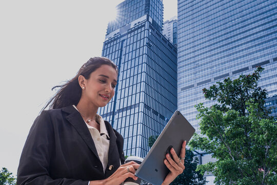 Indian female executive utilizing an AI-powered tablet for real-time financial data analysis and remote connectivity within a 5G smart city infrastructure environment. - Powered by Adobe