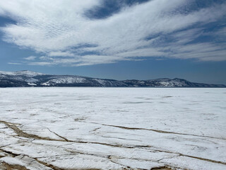A frozen bay in the Sea of ​​Okhotsk, Pacific Ocean. Cracked icy surface, snow covered hills, mountains. Winter landscape, north. Untouched nature photo. Background for tourism websites, advertising