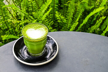 Close up view of hot matcha latte with black or grey table on the background. gray. copy space, empty, free, negative, text, design. Landscape. green leaves, plants. cafe, coffee shop. outdoor.