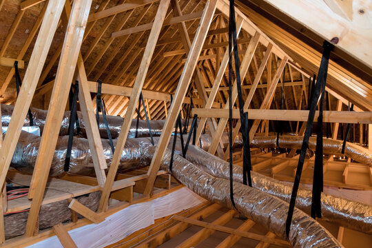 Workers are checking attic ductwork roof framing for proper installation ventilation during renovations.