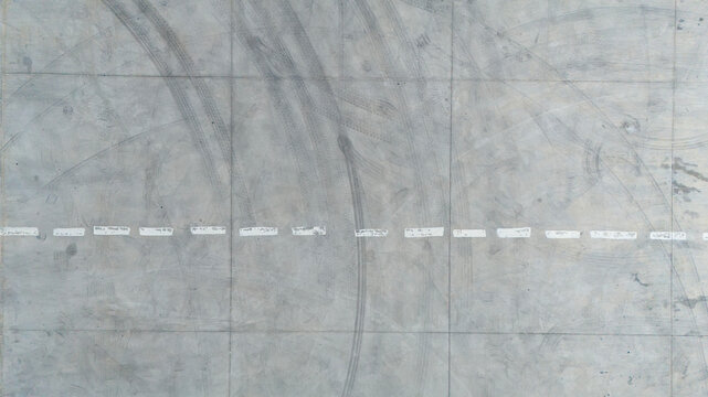 Top down aerial texture of a grey concrete parking lot with white lines and tire marks creating an urban industrial background