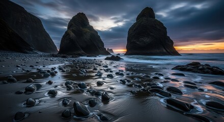 Dramatic seascape featuring towering rock formations at dusk along a pebble beach