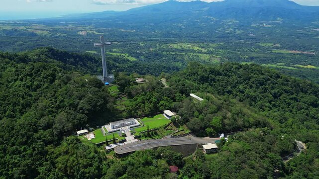 Pull‑out aerial revealing the towering Mt. Samat National Shrine as it recedes into view, framed by lush forested hills, valleys, and distant mountains in Pilar, Bataan, Philippines.