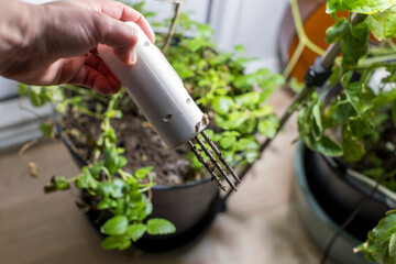 A hand holds a white, three-pronged soil testing device, checking the conditions of potting mix in an indoor planter.
