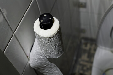 A textured roll of white toilet paper hangs on a black dispenser mounted to a light-colored tiled wall inside a bathroom.