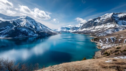 Obraz premium Majestic snowcapped mountains tower over a vast, deeply blue alpine lake under a bright sky