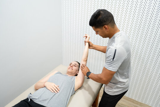 Hispanic physiotherapist assisting a female patient with arm stretching exercises, focusing on rehabilitation and recovery in a clinic - Powered by Adobe
