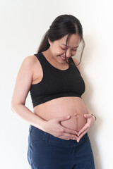 Beautiful young pregnant woman in good fit holds hands on her belly. Happy mother waiting for baby birth during pregnancy.