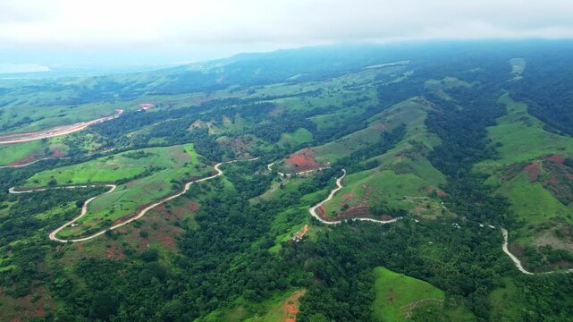 Forward aerial of the Bataanes in Bagac, Bataan, highlighting rolling green hills contrasted with bright winding roads cutting through the lush landscape toward the coastline.
