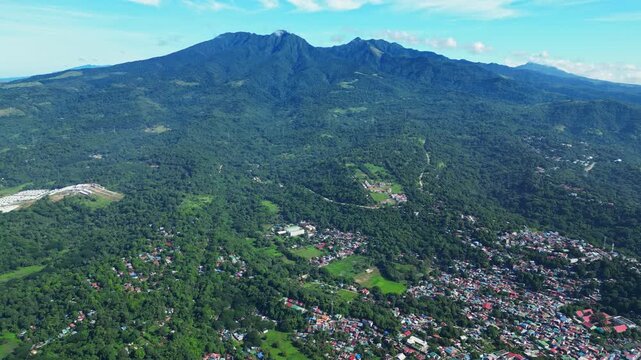 Aerial front view of Mount Mariveles in Bataan, showcasing its towering green peaks with the coastal town spread at the base, blending urban life and natural life.