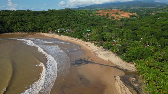 Rising aerial of Quinawan Beach in Mariveles, Bataan, showing turquoise waters rolling onto the sandy shore, with big waves creating white foam patterns along the coastline.