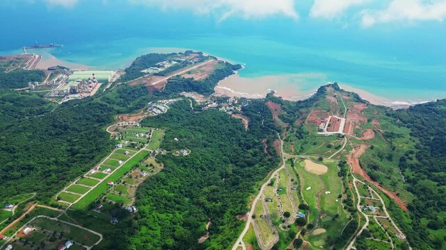 Sky‑high aerial of Tandatangan Signature Golf Course in Mariveles, Bataan, showing wide green fairways, winding roads, and surrounding hills leading toward the coastline.