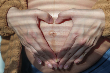A close-up photo of a pregnant woman making a heart shape on her large belly. Concept of pregnancy.