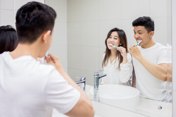 Happy young Asian couple brushing teeth together in the bathroom mirror