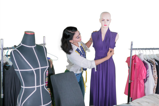 Female fashion designer adjusting a purple dress on a mannequin with white background