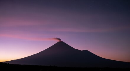 Erupting volcano silhouette under purple-pink twilight sky with visible stars