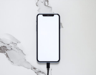 Smartphone with white screen charging on marble background, clean tech layout