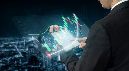 A businessman interacts with a digital tablet displaying financial graphs and data, set against a vibrant city skyline illuminated at night. Impute