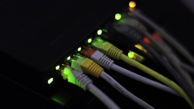 Colorful Ethernet cables plug into a networking device, illuminated by glowing green LED lights indicating active data transmission.