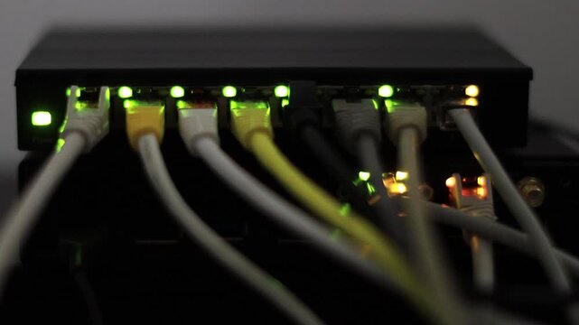 Multiple white and yellow Ethernet cables are plugged into a dark network switch, where blinking green and amber status lights indicate active data transmission connections.