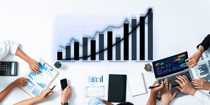 A diverse team collaborates in an office environment, utilizing laptops, charts, and calculators to analyze data and drive business growth with strategic insights. Axiom