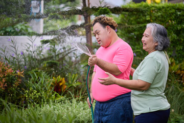 A happy moment of a senior woman and a young man with down syndrome holding a water hose in a...