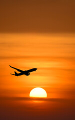 Vertical picture An aircraft soaring majestically into the sunset, with warm orange hues painting the sky. It's a silhouette shot