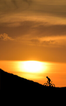 Vertical picture Silhouette of cyclist enjoying a sunset ride. The image captures the cyclist silhouetted against the bright sun