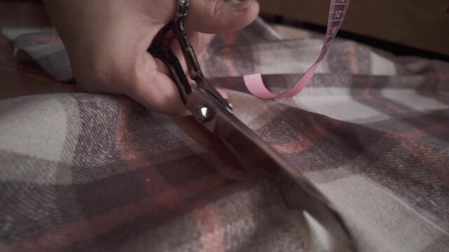 Close-up of a woman cutting previously measured fabric with precision scissors. A detailed look at the garment-making process, showcasing craftsmanship, accuracy, and the professional workflow in a se