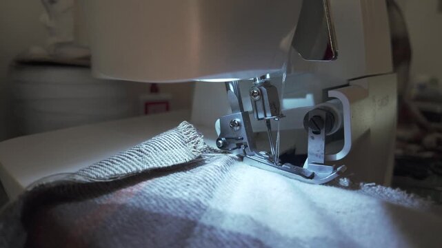 Close-up shot of fabric being sewn on an overlock machine, capturing the precise stitching of the edges. A detailed view of professional garment construction, highlighting craftsmanship and the clean 