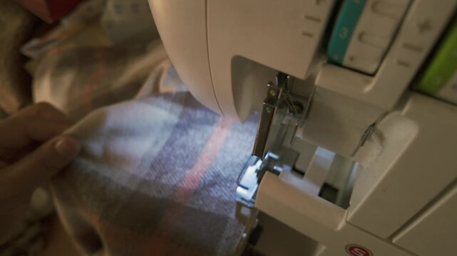 Close-up shot of fabric being sewn on an overlock machine, capturing the precise stitching of the edges. A detailed view of professional garment construction, highlighting craftsmanship and the clean 